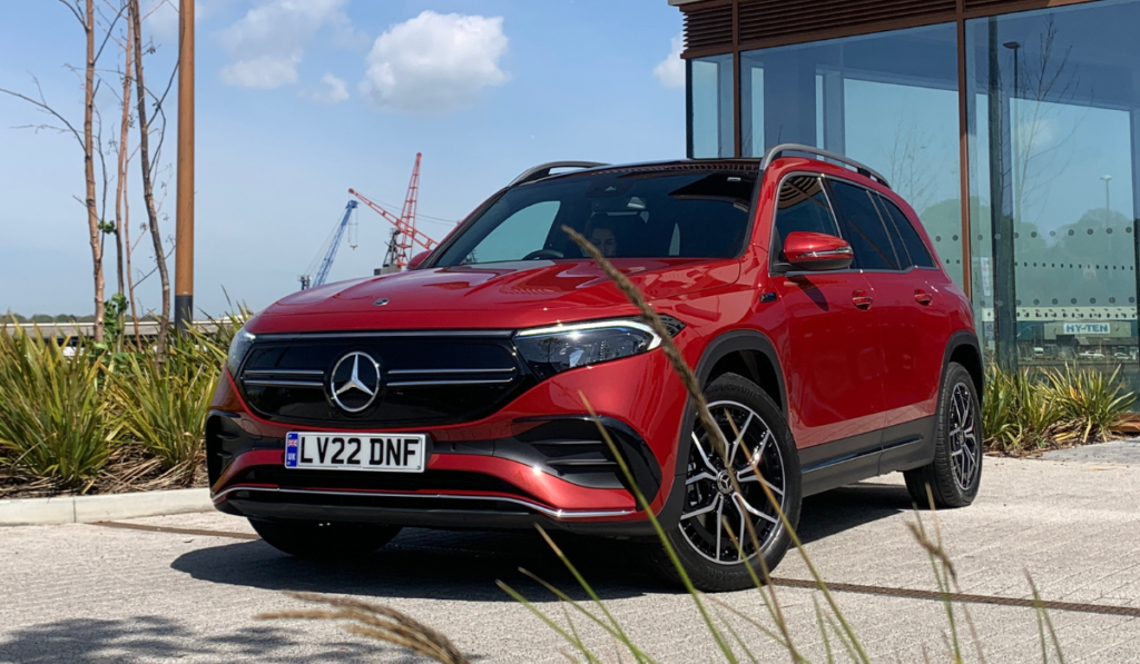 Red Mercedes EQB with blue skies and grass.
